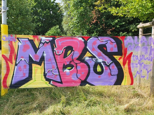 Eine Folie, die zwischen zwei Bäumen gespannt wurde und auf der die Buchstaben MBS stehen.