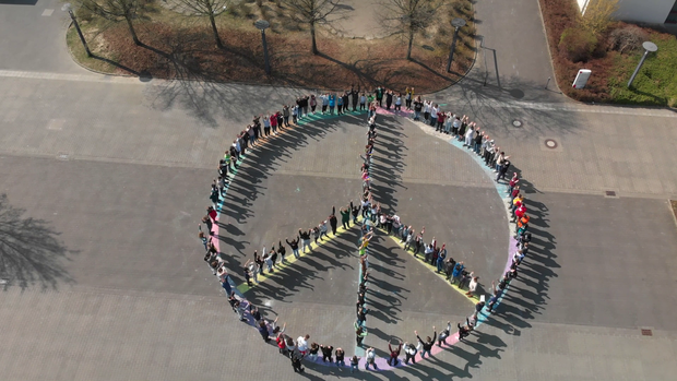 Ein Peace-Zeichen auf dem Schulhof, dass aus den Schüler:innen gebildet wird. Ein Peace-Zeichen auf dem Schulhof, dass aus den Schüler:innen gebildet wird.