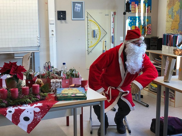 Der Weihnachtsmann sitzt neben einem festlich gedeckten Tisch in einem Klassenzimmer.