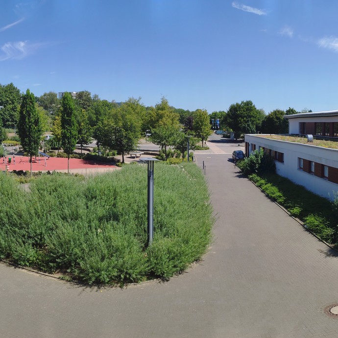 Auf der linken Seite ist ein Teil des Schulgebäudes. Daneben befindet sich der Schulhof. Auf der rechten Seite steht das Gebäude der Turnhalle. (vergrößerte Bildansicht wird geöffnet)